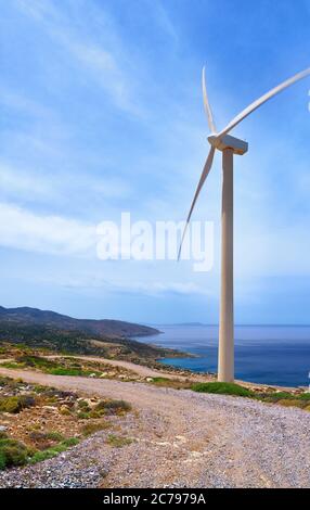 Einzelne Windmühle Turbine auf Hügel der Küste in bunten Landschaft gegen dynamischen blauen Himmel mit Wolken und gewundenen Straße. Stockfoto