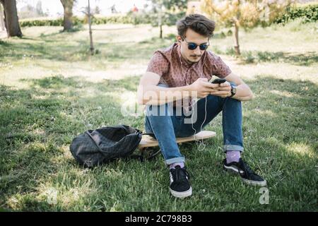 Attraktiver Mann mit Sonnenbrille, der im Wald Musik hört Stockfoto