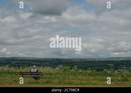 Single sitzende Figur auf einer Bank mit Blick auf die Landschaft und genießen die Aussicht Stockfoto