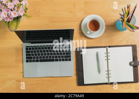 Ansicht von oben Laptop mit leerem Bildschirm, Bleistiften, Notizbuch, Vase und Tee auf dem Tisch im Home Office. Arbeitsplatz mit Laptop und Büromaterial. Stockfoto