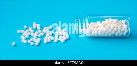 Bannerbild von homöopathischen Globuli in Glasflasche auf pastellblauem Hintergrund. Alternative Homöopathie Medizin Kräuter, Gesundheit und Pillen Konzept. Stockfoto