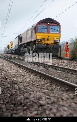 Die Diesellokomotive der Baureihe 66 in EWS-Lackierung schleppt die Ballastwagen der Network Rail auf einer Strecke der Eisenbahn in Großbritannien. Stockfoto