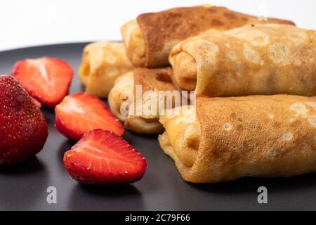 Hausgemachte Pfannkuchen mit Erdbeeren auf einem schwarzen Teller. Backen zu Hause, leckeres Frühstück. Stockfoto