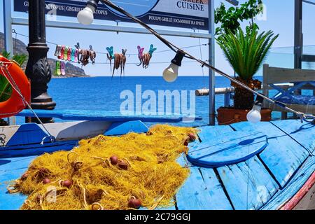 Outdoor Display, traditionelles Fischerboot, Fischernetz, sonnengetrocknete Oktopusse am Seil, blaues Meer und typisch griechische Hügel im Hintergrund, Kreta, Griechenland Stockfoto