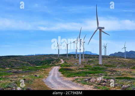 Windmühle Turbinenfarm auf einem Hügel in farbenfroher Landschaft mit gewundener Straße gegen blauen Himmel an klaren sonnigen Sommertag. Stockfoto