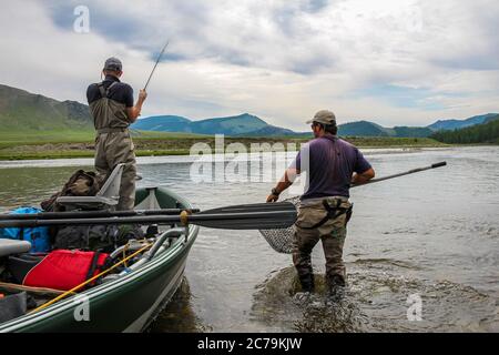 Ein Fliegenfischer mit einer Taimenforelle am Ende seiner Linie von einem Boot aus, auf dem Delger Moron Fluss in der Mongolei, Moron, Mongolei - 14. Juli 2014 Stockfoto