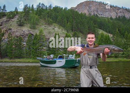 Ein Fliegenfischer, der stolz eine Taimenforelle hält, gefangen auf dem Delger Moron Fluss in der Mongolei, Moron, Mongolei - 14. Juli 2014 Stockfoto