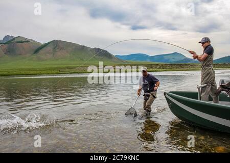 Ein Fliegenfischer mit einer Taimenforelle am Ende seiner Linie von einem Boot aus, auf dem Delger Moron Fluss in der Mongolei, Moron, Mongolei - 14. Juli 2014 Stockfoto