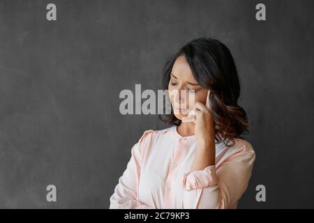 Junge Geschäftsfrau, die gestresst aussieht, während sie mit geschlossenen Augen und einem Finger auf ihrem Tempel vor einem Kreidetafel-Hintergrund steht Stockfoto
