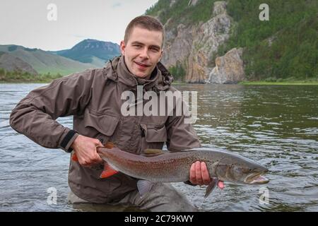 Ein Fliegenfischer, der stolz eine Taimenforelle hält, gefangen auf dem Delger Moron Fluss in der Mongolei, Moron, Mongolei - 14. Juli 2014 Stockfoto