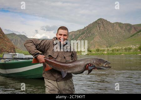 Ein Fliegenfischer, der stolz eine große Trophäe mit Taimenforelle hält, gefangen auf dem Delger Moron Fluss in der Mongolei, Moron, Mongolei - 14. Juli 2014 Stockfoto