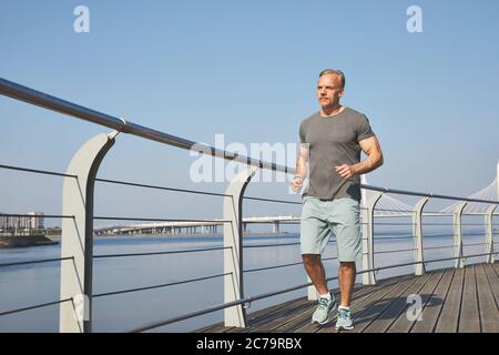 Sportlich reifer Mann in Shorts Joggen auf Stadtdamm am Morgen, gesundes Lifestyle-Konzept Stockfoto