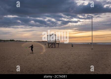 Kleiner Junge mit Spaten neben einer Rettungshütte am Strand bei Sonnenuntergang Stockfoto