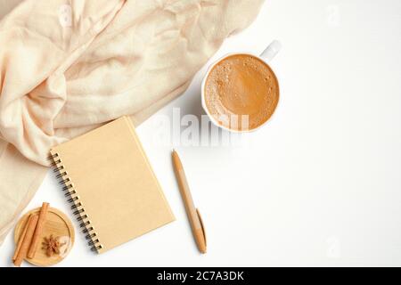 Gemütlicher Schreibtisch mit beigefarbenem Schal, Tasse Kaffee, Notizbuch, Zimtstangen. Herbst- oder Winterkonzept. Flach liegend, Draufsicht. Stockfoto