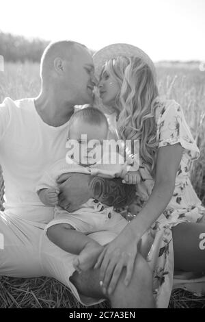Glückliche junge Eltern mit Baby ruht zwischen Weizenfeld und sie küsst. Schwarzweiß-Bild. Stockfoto
