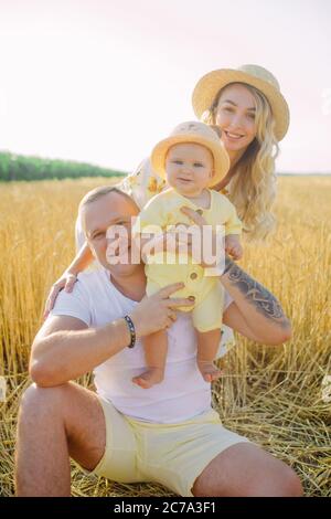 Glückliche junge Familie mit Baby sitzt und ruht zwischen gelben Weizenfeld. Stockfoto