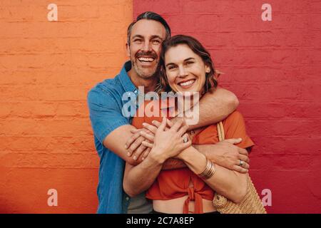 Portrait von liebevollen reifen Paar umarmen einander vor rotem und orangenen Hintergrund und lächelnd. Stockfoto