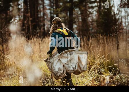 Mann, der im Wald arbeitet, um neue Bäume zu Pflanzen, durch trockenes Gras zu gehen, das Beutel voller neuer Sämlinge trägt. Mann, der in der Forstwirtschaft Bäume in defo Pflanzen Stockfoto