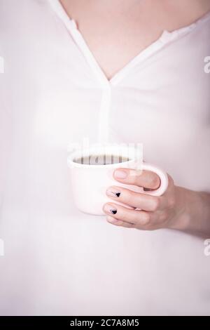Weibliche Hände halten rosa Tasse schwarzen Tee auf rosa Hintergrund. Natürliche Maniküre mit Dreieckmuster Stockfoto