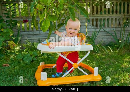 Baby Mädchen im Garten in einem Wanderer lernt zu gehen, die ersten Schritte in einem Wanderer Stockfoto