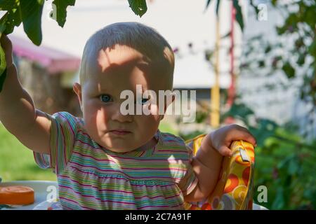 Ein schönes Baby versteckte sich vor der Hitze unter einem Baum, Schatten auf dem Gesicht eines überraschten Mädchens Stockfoto