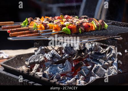 Gegrillte Grillspieße von Gemüse und Fleisch auf dem Grill im Freien. Leuchtende Kohle sichtbar. Stockfoto
