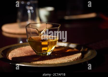 Auf einem dunklen Tisch ist eine kleine Glas Teekanne mit Bernstein Tee in ihm Stockfoto