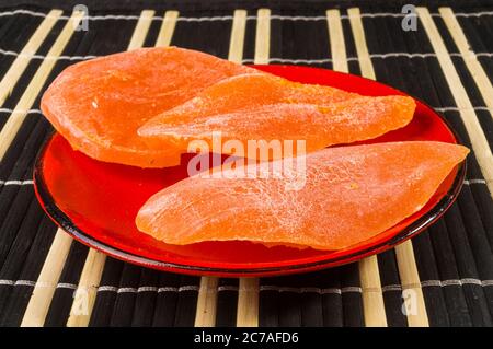 Scheiben getrocknete Mango in einer roten Untertasse auf einer Bambusmatte, Nahaufnahme. Stockfoto