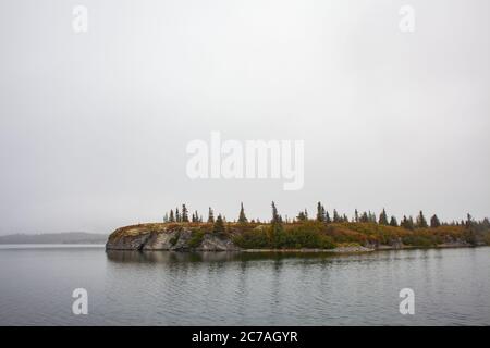 Eine ruhige, bewaldete Insel liegt umgeben von ruhigem, nebelhaltigem Wasser in der Wildnis Alaskas, die die ruhige und unberührte Schönheit der abgelegenen Natur einfängt. Stockfoto