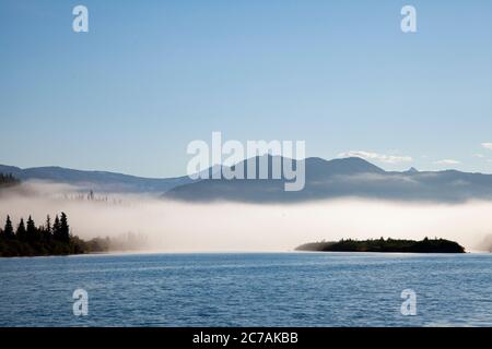 Der Morgennebel zieht über den Lake Iliamna, Alaska, mit Bergen im Hintergrund und Sonnenlicht, das sich vom ruhigen, ruhigen Wasser der Wildnis reflektiert Stockfoto