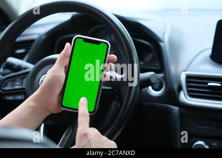 Über die Schulter des Mannes tippen grünen Bildschirm Smartphone im Auto. Weichzeichnen Hintergrund Stockfoto