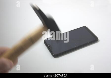Nahaufnahme eines beweglichen Hammers, der den Bildschirm eines Mobiles, das auf einem weißen Tisch isoliert ist, gebrochen hat Stockfoto