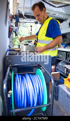 15. Juli 2020, Mecklenburg-Vorpommern, Bentin: Auf einer Baustelle für Breitband-Internet-Erweiterung bläst der Glasfasertechniker Marc Klöpping ein Glasfaserkabel durch ein leeres Rohr zu einem mehrere hundert Meter entfernten Hausanschluss. Die Firma WEMACOM verlegt derzeit Glasfaserverbindungen im Landkreis Nordwestmecklenburg. Bisher wurden rund 5,500 Hausanschlüsse für den Anschluss an das schnelle Glasfasernetz vorbereitet. Mecklenburg-Vorpommern erhält rund 850 Millionen Euro aus dem Bundesprogramm für den Breitbandausbau in unterversorgten ländlichen Regionen Stockfoto