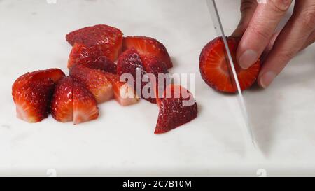 Frau schneidet frische reife Erdbeeren zum Dessert, Nahaufnahme auf weißem Hintergrund Stockfoto