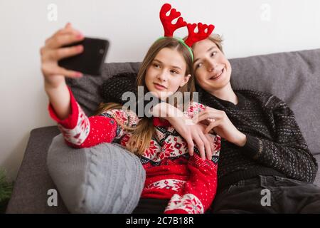 Porträt eines jungen lächelnden Paares, das zu Hause auf dem Sofa sitzt und ein lustiges Selfie macht, während man Zeit miteinander verbringt Stockfoto