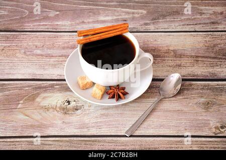 Auf einer Untertasse auf einem Holztisch steht eine Tasse schwarzen Kaffee mit Zimtanis und Scheiben braunem Rohrzucker. Nahaufnahme. Stockfoto
