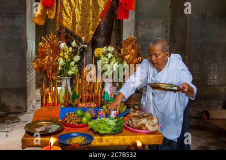 Eine buddhistische Nonne ordnet Opfergaben an der Basis einer dekorierten Statue von Herrn Vishnu, einem Hindu-gott, dem Obersten Gott des Vaishnavismus (einer der drei Stockfoto