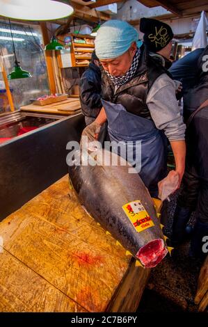 Ein Mann bereitet einen Gelbflossenthun für den Verkauf auf dem Tsukiji Fischmarkt in Tokio, Japan, vor. Stockfoto