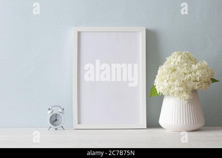 Ein Strauß weißer Hortensien steht an der blauen Wand auf einem Holztisch. A4-Rahmen steht aufrecht. Bündel. Stockfoto