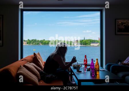 Menschen genießen den Blick auf den Mälarsee, essen eine Mahlzeit und trinken aus farbigen Flaschen. Blick auf die großen Panoramafenster im Cafe oben Stockfoto