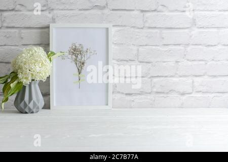 Grüne Hortensien in einer grauen Vase im nordischen Stil stehen auf einem weißen Holztisch. Background alten Ziegel. Paket, Kopierbereich. Stockfoto