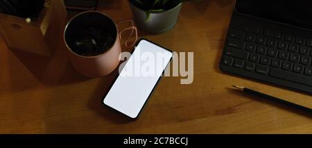 Zugeschnittene Aufnahme eines Mock-up-Smartphones auf einem rustikalen Arbeitsplatz mit digitalem Tablet, Becher und Zubehör Stockfoto