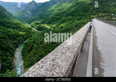 Junge auf Durdevica Brücke mit Blick auf den schönen smaragdgrünen Fluss Tara im Norden Montenegros. Seitenansicht von oben von fliegender Drohne Stockfoto