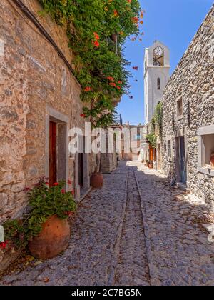 Rote Blumen und rauer Stein. Eine schmale Straße mit alten Häusern in Pyrgi Kleinstadt, Chios Insel, Griechenland. Alles ist aus Stein, aber grünes Laub Stockfoto