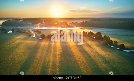 Sonnige Sommer ruhige Morgen Panorama. Kleiner Fluss, Nebel Sonnenaufgang Luftbild. Erste Sonnenstrahlen über grüne Wiese und Feld Stockfoto