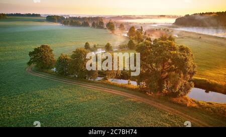 Sonnige Sommer ruhige Morgen Panorama. Kleiner Fluss, Nebel Sonnenaufgang Luftbild. Erste Sonnenstrahlen über grüne Wiese und Feld Stockfoto