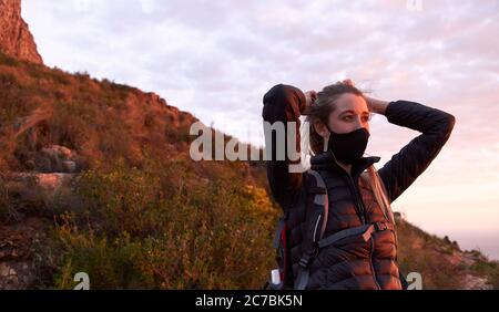 Junge Frau Anpassung Gesichtsmaske auf der Spitze des Berges während des Sonnenuntergangs Stockfoto