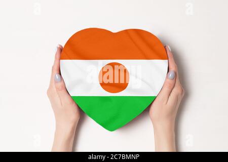 Flagge Nigers auf einem herzförmigen Kasten in einer weiblichen Hand. Weißer Hintergrund Stockfoto