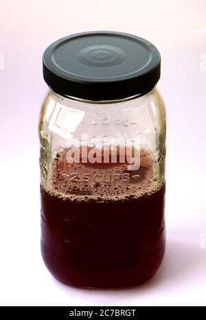 Versiegeltes Klarglas-Messglas mit vier Messmethoden und einem schwarzen Metalldeckel mit dunkelrotem Waldfruchtsaft, halb voll oder halb leer Stockfoto