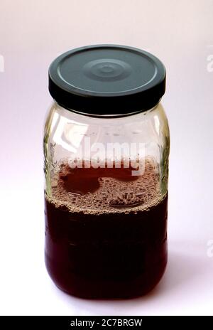 Versiegeltes Klarglas-Messglas mit vier Messmethoden und einem schwarzen Metalldeckel mit dunkelrotem Waldfruchtsaft halb voll oder halb leer Pint Stockfoto